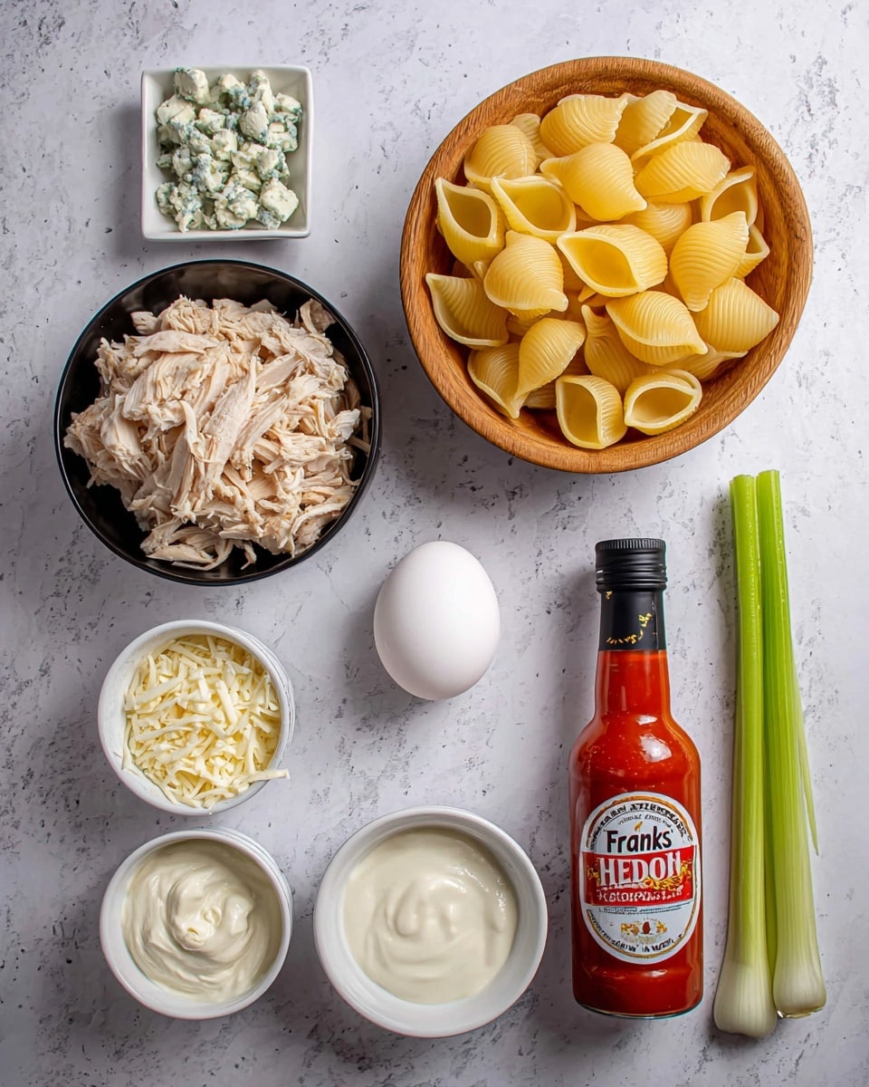 The image shows an arrangement of cooking ingredients on a white marbled surface. At the top right, there is a wooden bowl filled with large, yellow uncooked pasta shells. Below the bowl, there is a black bowl holding shredded light brown cooked chicken. To the left of the chicken, there are three white small round bowls stacked vertically: shredded white cheese on top, smooth white ricotta cheese in the middle, and creamy sour cream at the bottom. Between the chicken and cheese bowls, a white egg is placed in the center. To the right of the egg, there is a bottle of bright red hot sauce with a black cap and a label reading