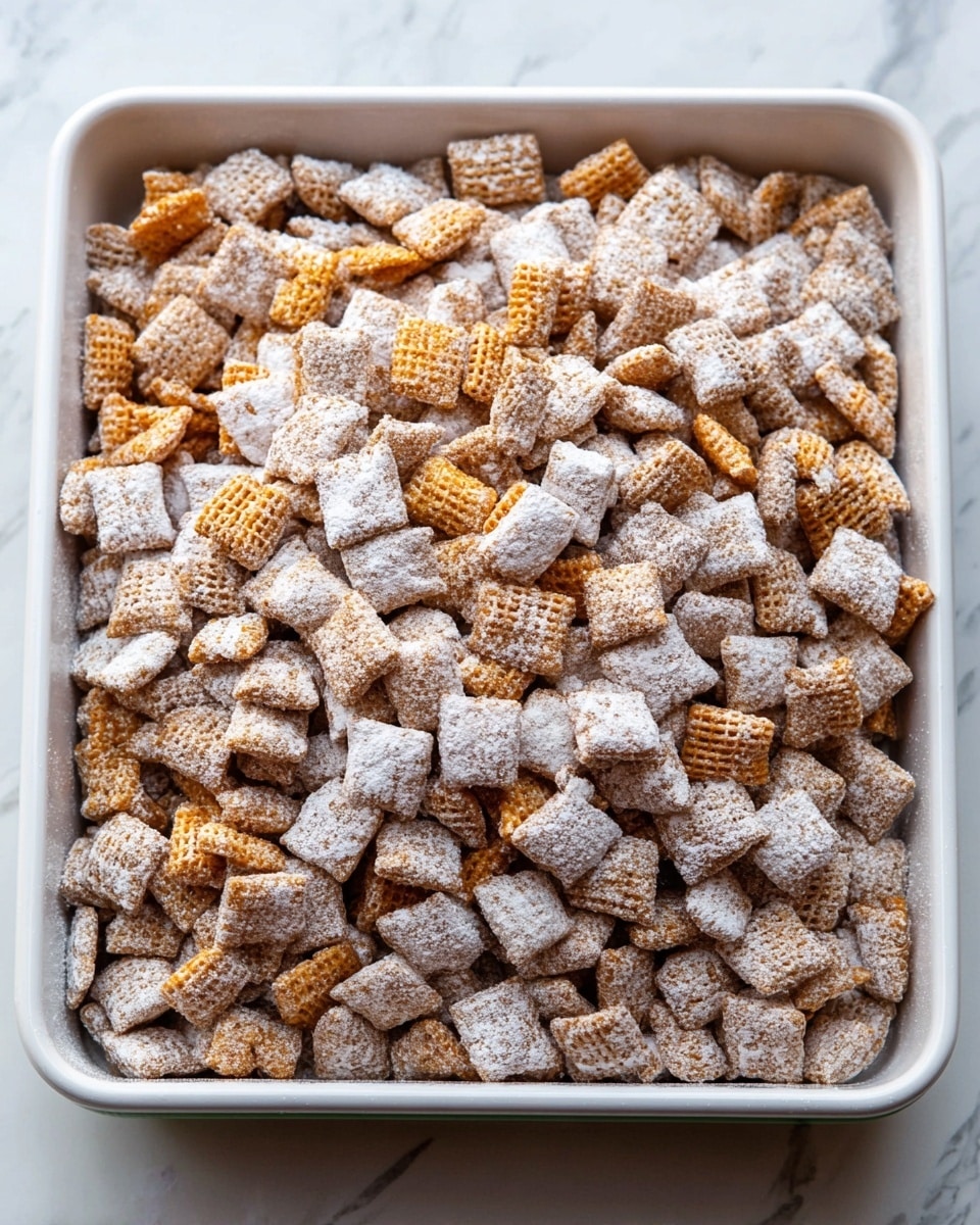 The image shows a deep square white tray filled with many small square cereal pieces. The cereal is mostly light brown but dusted heavily with white powdered sugar, covering the surface with a snowy look. Some of the cereal squares have small holes and are slightly more orange in color, scattered evenly throughout. The tray is placed on a white marbled surface which adds a clean background. Photo taken with an iphone --ar 4:5 --v 7