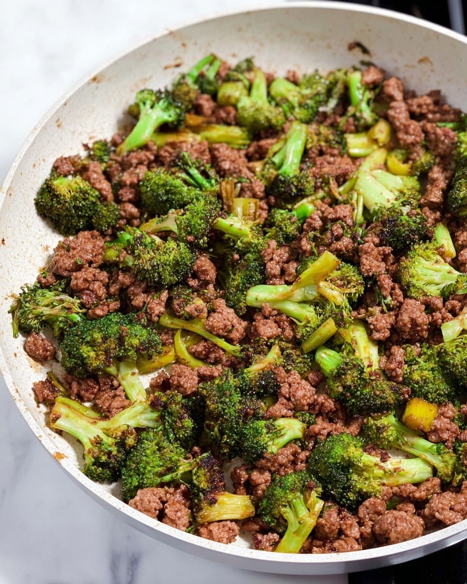 A white pan filled with cooked ground meat and broccoli mixed together. The ground meat is crumbly and browned, spread evenly across the pan. Bright green broccoli florets and small stalk pieces are scattered among the meat, showing a slight char and softness from cooking. The mixture looks hot and freshly cooked, sitting on a white marbled stove surface. photo taken with an iphone --ar 4:5 --v 7