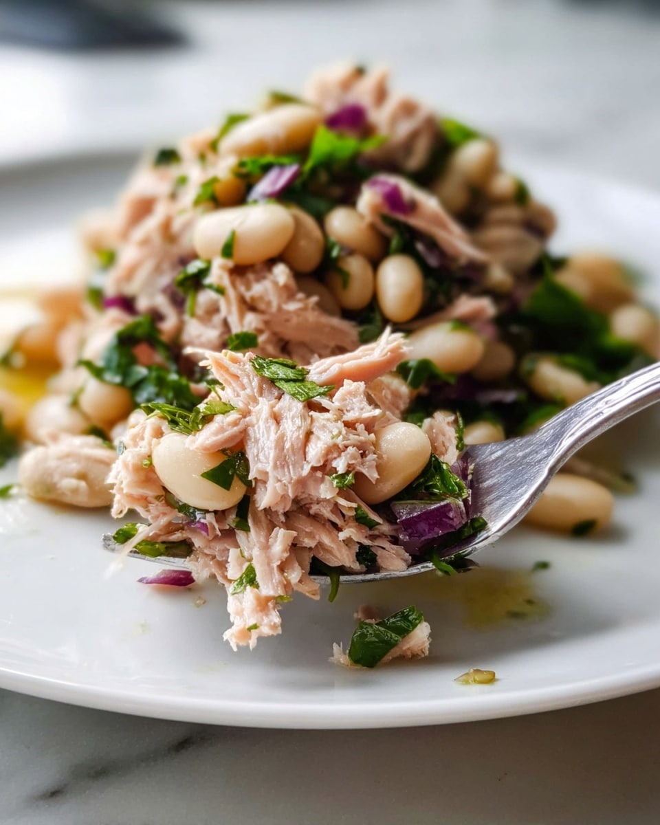The dish is presented on a white bowl sitting on a white marbled surface, featuring a pile of mixed ingredients layered in a natural and rustic style. The base layer includes plump, smooth white beans scattered across the plate, giving a creamy pale texture. On top of the beans, there are chunks of light pink salmon mixed with finely chopped green herbs and scattered purple-red onion pieces. A glossy, light oil dressing glistens over the beans and salmon, enhancing the colors and adding a slight shine. The salmon pieces have a soft, flaky texture with visible rind marks, while the herbs and onion add fresh, crisp green and purple accents throughout the dish. The image is bright with natural lighting, focusing closely on the details of the ingredients, photo taken with an iphone --ar 4:5 --v 7