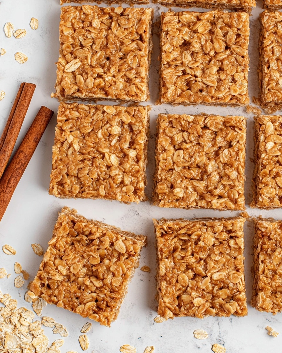 The image shows nine square oat bars arranged neatly in a grid on a white marbled surface. Each bar has a rough texture made of large oat flakes bound together by a sticky, light brown mixture, giving them a dense and chewy look. Two brown cinnamon sticks are placed diagonally on the left side, partially resting on the bars and the surface, adding a warm brown color contrast. The oat bars have slightly uneven edges, showing the natural oats layered closely together. The background has a subtle white marbled look with small scattered oat flakes around the bars. photo taken with an iphone --ar 4:5 --v 7