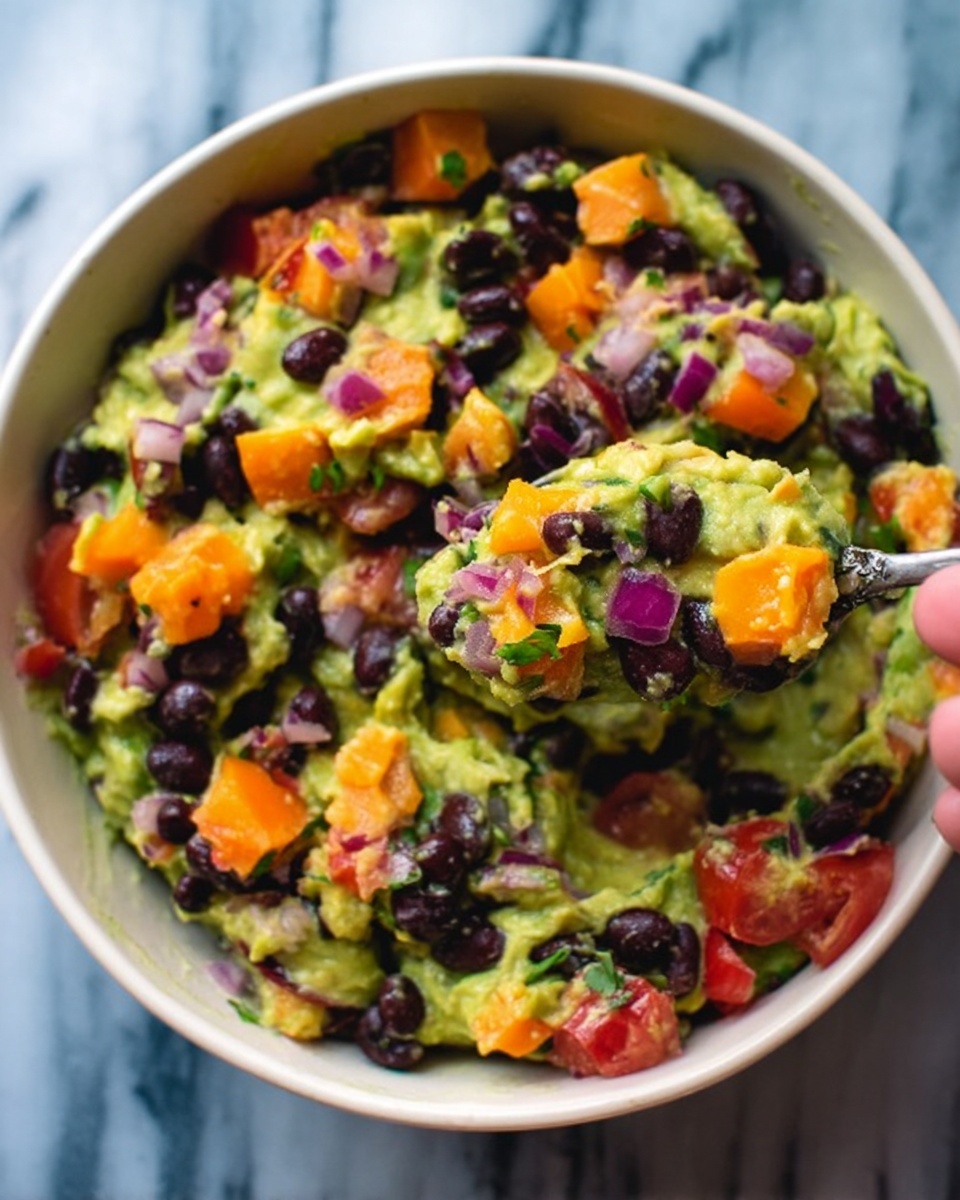 The image shows a close-up of a white bowl filled with a colorful mixture of mashed avocado, black beans, diced orange bell peppers, chopped red onions, and small pieces of red tomatoes. The creamy green avocado forms the base with a chunky texture, dotted with smooth dark black beans and bright orange and red vegetable pieces scattered throughout. The bowl sits on a white marbled surface. The photo is taken with a woman's hand holding a spoon scooping some of the mix. Photo taken with an iphone --ar 4:5 --v 7