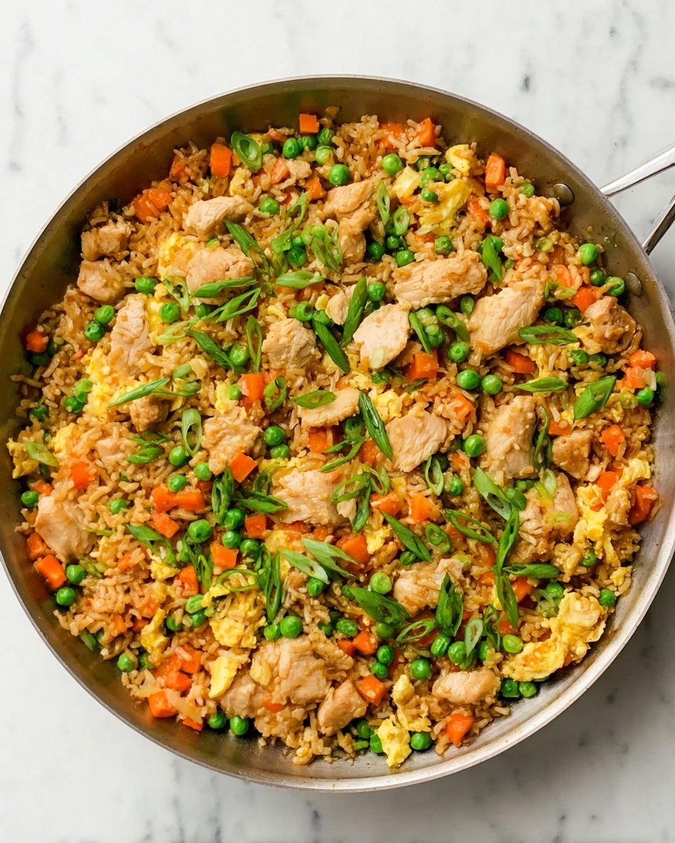 The image shows a large skillet filled with a colorful fried rice dish layered evenly with light brown cooked rice mixed with bright green peas, small orange carrot cubes, and light yellow scrambled egg pieces scattered throughout. Chunky pieces of light golden cooked chicken are spread across the dish, topped with thin slices of fresh green onion. The skillet sits on a white marbled surface. Photo taken with an iphone --ar 4:5 --v 7