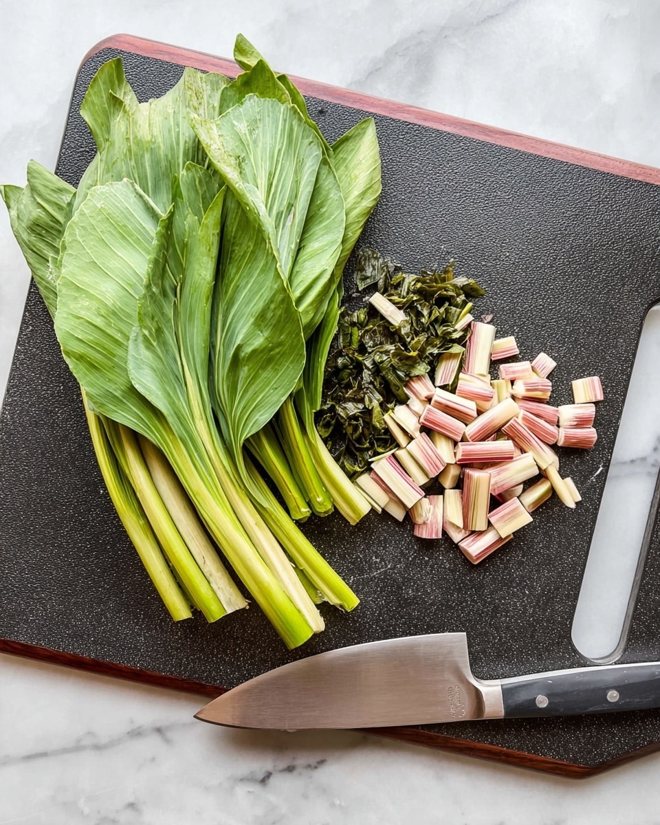 A dark cutting board with a reddish border sits on a white marbled surface, holding fresh green leafy stalks and small chopped pieces at the right side. The leafy greens are stacked in layers, showing bright green hues with a smooth texture, while the cut pieces transition into shades of pale pink, cream, and green, reflecting the plant's stem ends. A large knife with a shiny silver blade and a black handle rests on the right side of the cutting board. photo taken with an iphone --ar 4:5 --v 7