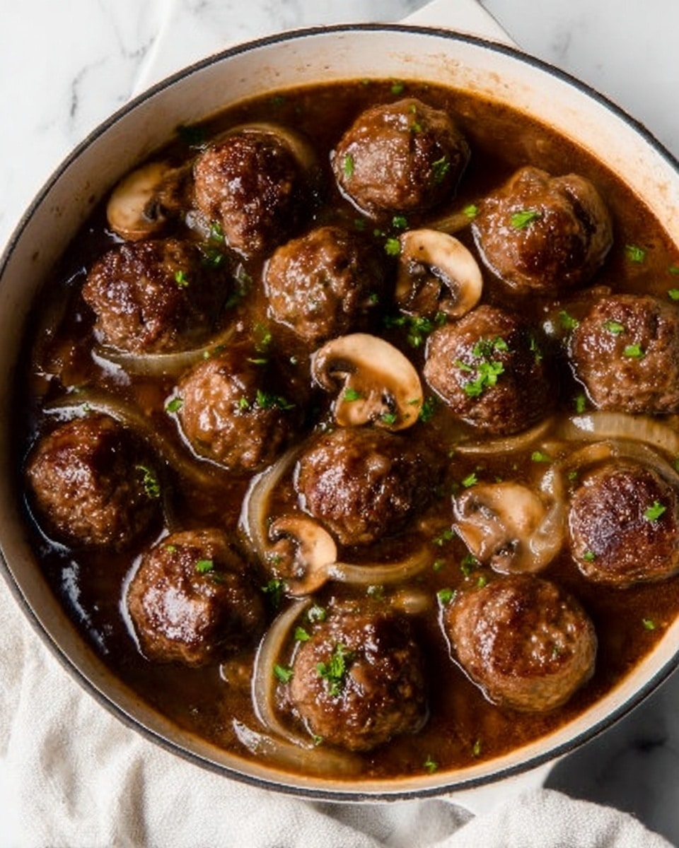 A white pan filled with a rich brown sauce, containing round meatballs evenly spread inside. Thinly sliced light brown mushrooms and soft cooked onions float in the sauce, with small bits of green herbs sprinkled on top. The sauce has a glossy texture and fills about three-quarters of the pan, while the meatballs sit mostly above the sauce. The pan rests on a white marbled surface. Photo taken with an iphone --ar 4:5 --v 7