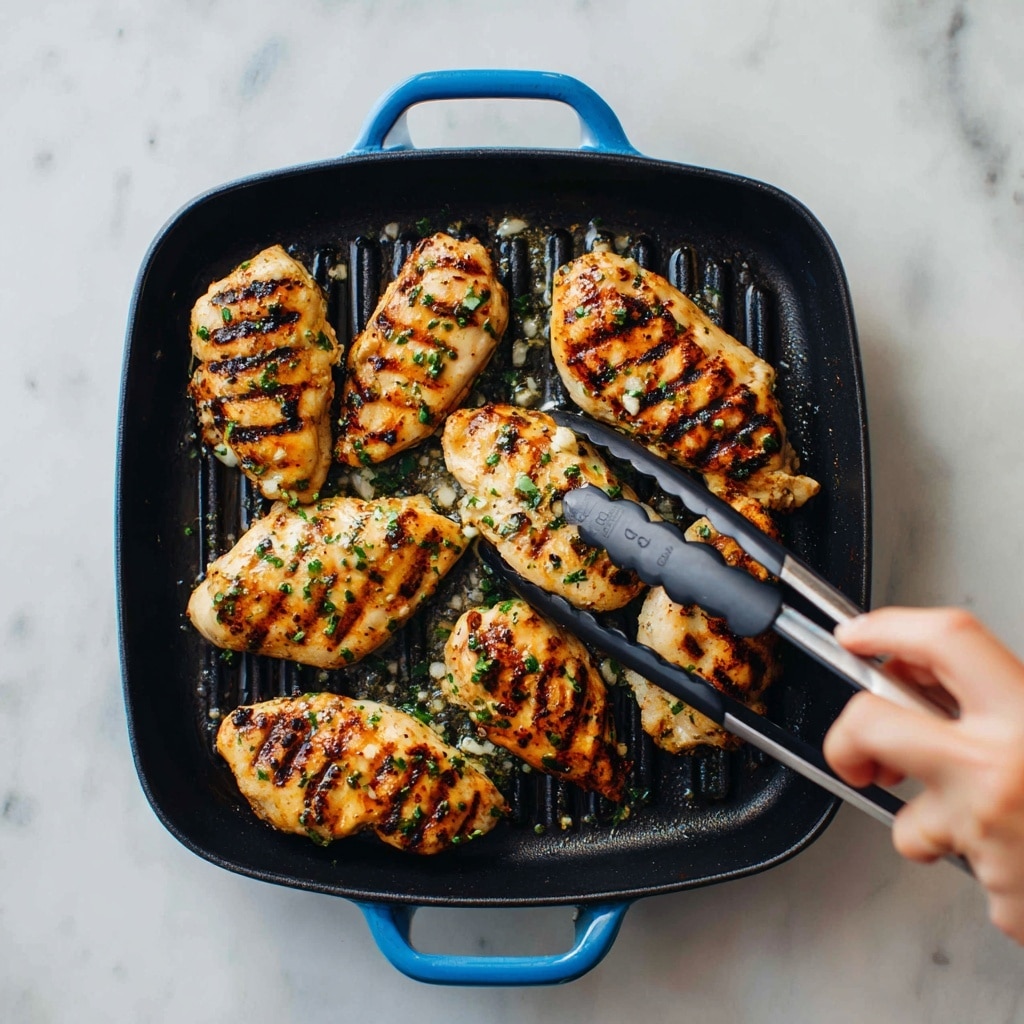 Inside a black square pan with blue handles, several pieces of grilled chicken are cooking. The chicken pieces are light brown with visible grill marks and small green herbs sprinkled on top. Some parts of the chicken have a slight char for texture. Bubbles of oil are sizzling around the chicken pieces in the pan. A woman's hand holding black tongs is lifting one piece of chicken on the right side of the pan. The background is a white marbled texture. photo taken with an iphone --ar 4:5 --v 7