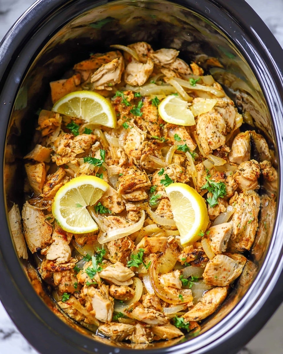 The image shows a large silver slow cooker filled with chopped cooked chicken pieces that have a golden brown color and a slightly crispy texture. Scattered on top are thin, translucent, cooked onion slices with a mild yellow tint, along with small green parsley leaves adding fresh color. There are also several lemon wedges with bright yellow rind and pale yellow flesh placed evenly inside the slow cooker, blending with the warm tones of the chicken and onions. The background is a white marbled texture. Photo taken with an iphone --ar 4:5 --v 7
