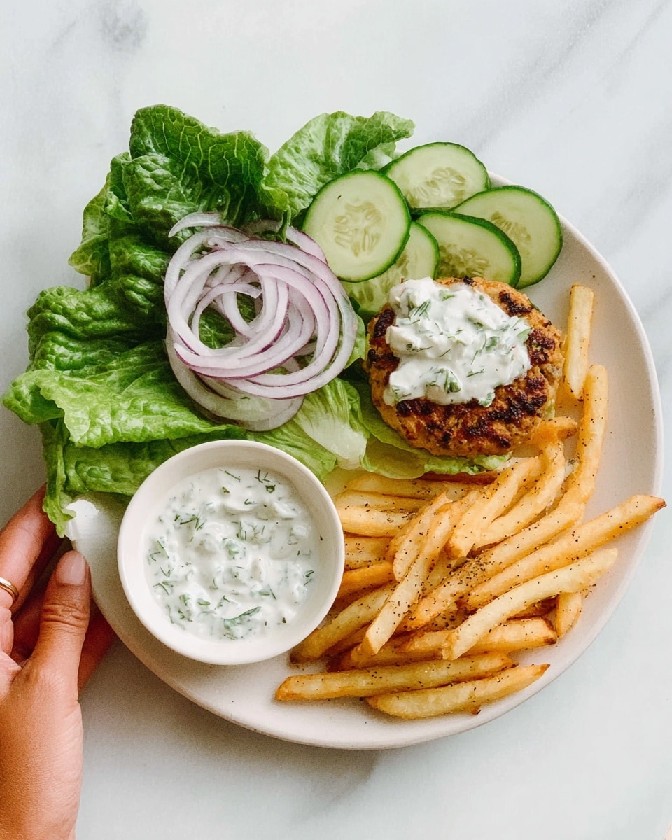 The image shows a white plate with three main parts on a white marbled surface. On the left side, there are fresh green lettuce leaves topped with thin rings of purple onion and slices of pale green cucumber. In the center, slightly to the right, there is a golden-brown patty with a soft, white dollop of sauce seasoned with green herbs. On the far right, there are light golden french fries, sprinkled with some seasoning. A woman’s hand is holding a small white bowl filled with a white sauce that has green herbs visible in it. photo taken with an iphone --ar 4:5 --v 7
