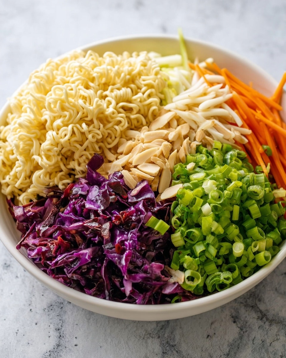 A white bowl shows a colorful layered salad with five main parts. At the top left, there is a big pile of light yellow, dry ramen noodles with a wavy texture. To the right of the noodles, thin orange carrot sticks are stacked in the background, while thin beige slivered almonds are beside them. Below the carrots and almonds, bright green chopped scallions form a thick mound on the bottom right. Next to the scallions on the left, there is a heap of finely shredded dark purple cabbage with a glossy look. The bowl sits on a white marbled surface. Photo taken with an iphone --ar 4:5 --v 7