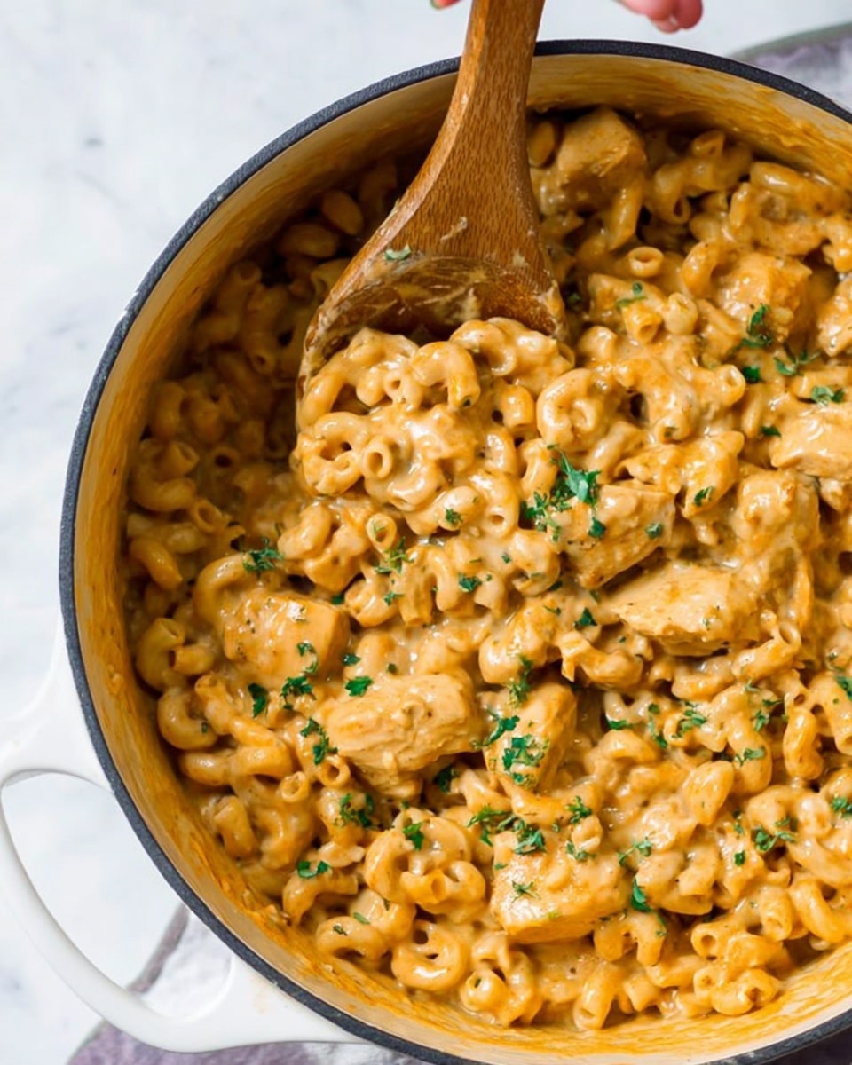 A white pot filled with creamy macaroni and chicken mixture with tan-colored sauce, showing three visible pieces of cooked chicken covered in sauce, surrounded by elbow pasta coated in the same sauce. There are small green herb pieces sprinkled on top for garnish. A wooden spoon is dipped into the pot, scooping some of the pasta and chicken, and a woman's hand is partly visible holding the spoon from the left side. The background is a white marbled surface. Photo taken with an iphone --ar 4:5 --v 7