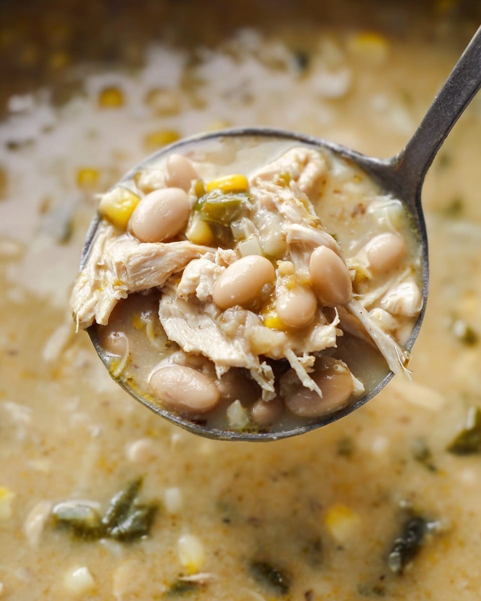 The image shows a white bowl filled with creamy chicken and corn soup. The soup has a thick texture with visible chunks of light-colored chicken, yellow corn kernels, and small green herbs scattered throughout. On top, there is a layer of shredded melted cheese in a pale orange color. A spoon holds a scoop of the soup close to the camera, showing the creamy and textured mix with pieces of chicken, corn, and cheese. Behind the soup, there are crispy pale yellow tortilla chips partially dipped in the soup, and a green cilantro leaf adds a fresh touch on top. The setting is on a white marbled surface. photo taken with an iphone --ar 4:5 --v 7