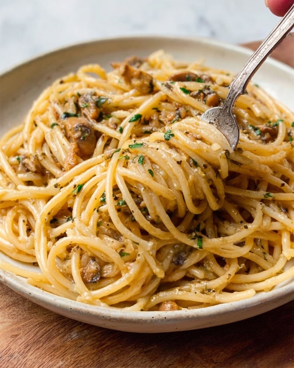 A close-up view of a white ceramic plate filled with thick spaghetti pasta twisted around a silver fork held by a woman's hand on the left side. The pasta is coated in a glossy light brown sauce with small pieces of sautéed mushrooms and herbs scattered evenly throughout. The dish sits on a wooden surface that transitions to a white marbled texture in the background. The sauce gives the pasta a shiny, slightly oily look, and the pasta strands are thick and slightly curved, showing a soft texture. photo taken with an iphone --ar 4:5 --v 7