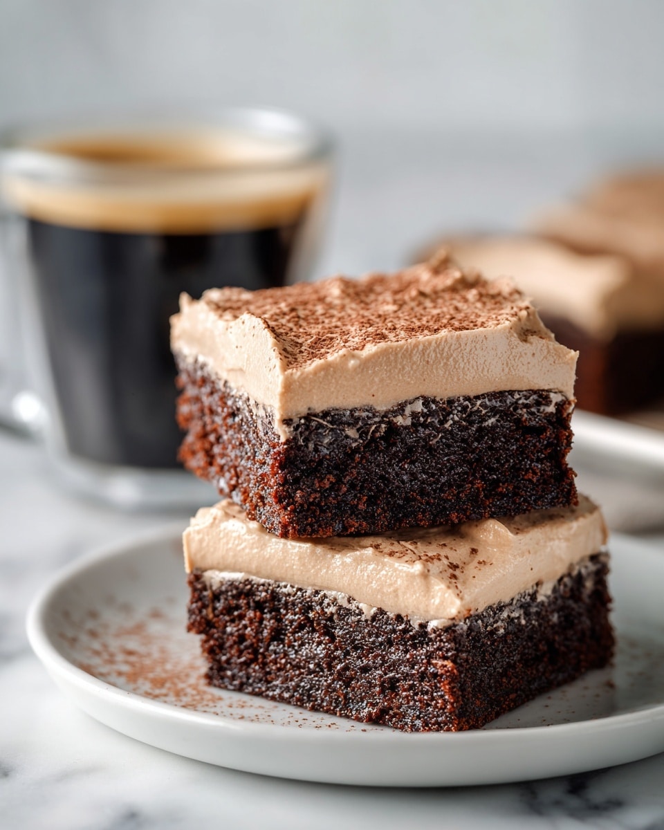 A stack of three square chocolate brownies with a thick layer of light brown frosting on top. Each brownie layer is dark brown, moist, and dense, with the smooth frosting layer evenly spread above. The top frosting has a slight dusting of cocoa powder. The brownies are placed on a white plate on a white marbled surface, with a clear glass cup of black coffee blurred in the background. photo taken with an iphone --ar 4:5 --v 7