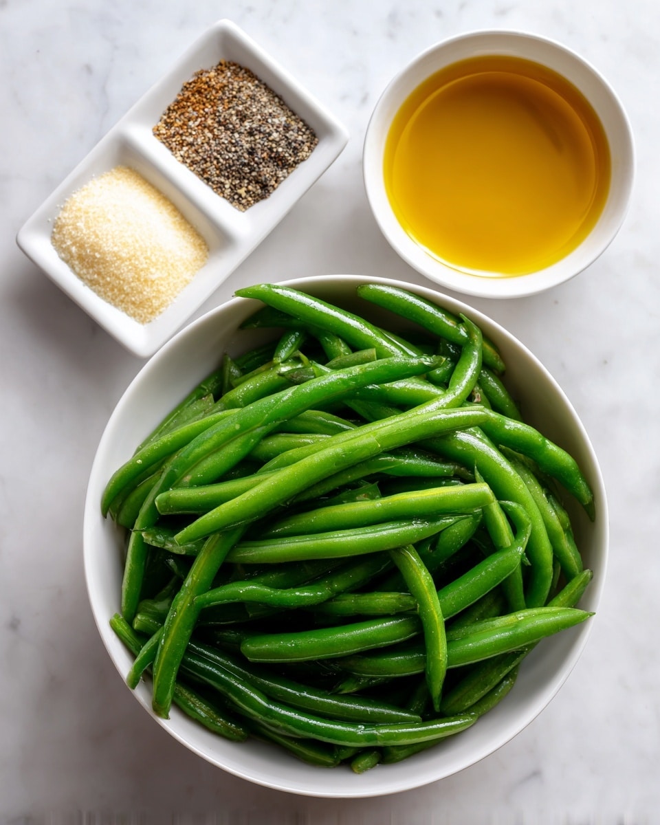 The image shows three separate containers on a white marbled surface. The largest container is a white bowl filled with fresh green beans that have a smooth, glossy texture and vibrant green color, layered evenly within the bowl. Above and to the right of this bowl is a small white bowl with golden olive oil that has a shiny, smooth surface. To the left side of the olive oil, there is a small white square dish divided into three sections, each holding a different powder or granule: pale yellow garlic powder, white salt, and black and white mixed salt and pepper. The composition is simple and clean, with a focus on the fresh ingredients. Photo taken with an iphone --ar 4:5 --v 7