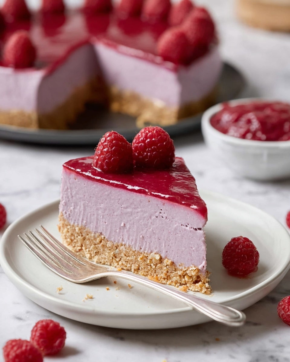 A slice of raspberry cheesecake is shown on a white plate placed on a white marbled surface. The cake has three layers: a light brown crumbly base, a thick middle layer of smooth light purple filling, and a shiny red raspberry topping. Two fresh raspberries are placed on top of the slice. A silver fork rests on the plate beside the cake, and scattered raspberries and crumbs lie on the surface nearby. In the blurred background, a whole cheesecake with similar layers and fresh raspberries on top sits on a dark tray, with a small white bowl filled with the red topping also visible. Photo taken with an iphone --ar 4:5 --v 7