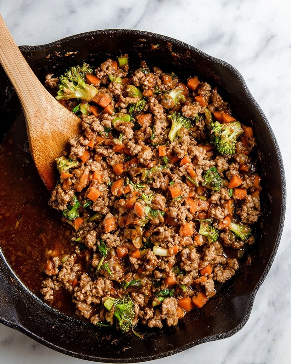 In a black cast iron skillet on a white marbled background, there is a mix of cooked ground meat with small pieces of orange carrots and green broccoli florets, all coated in a dark brown sauce. A wooden spatula is partly stiring the mixture from the left side, showing a mixture thick with chunks of meat and vegetables evenly spread across the skillet. The sauce pools slightly on one side, giving a glossy texture to the dish photo taken with an iphone --ar 4:5 --v 7
