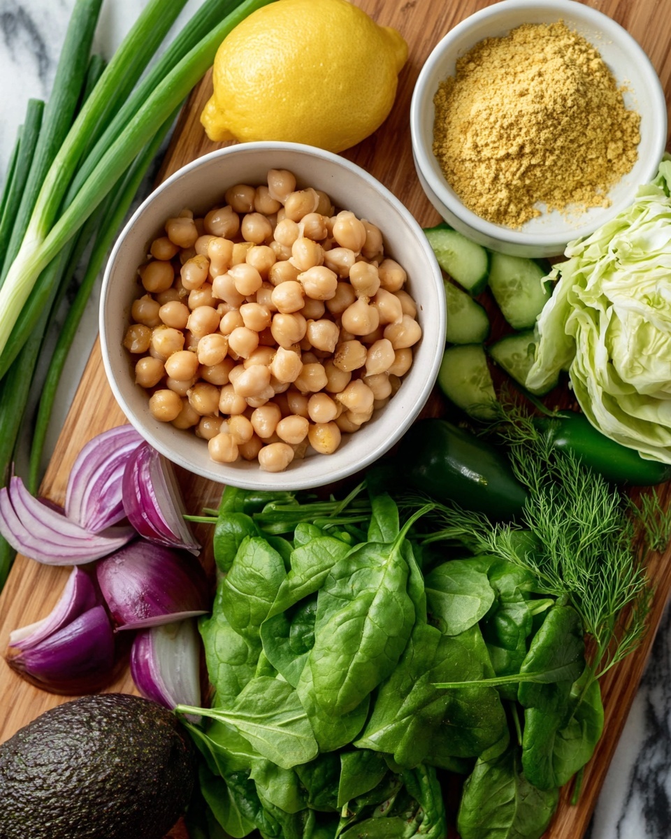 The image shows a white bowl filled with round, light beige chickpeas in the bottom left corner, placed on a wooden table with a white marbled texture background. Around the bowl are fresh green spinach leaves with visible stems, a small bunch of green dill, and a few long green spring onions lying on the top left edge. There is a halved lemon with a bright yellow inside and a cucumber sliced in half, showing its dark green rough skin and lighter green inside. A dark green jalapeño pepper lies near the center, beneath a wedge of light green cabbage at the top. A white bowl filled with yellow nutritional yeast flakes is placed toward the right side above the spinach, next to a dark, textured avocado. There is also a few pieces of sliced purple onion near the bottom left center. Photo taken with an iphone --ar 4:5 --v 7