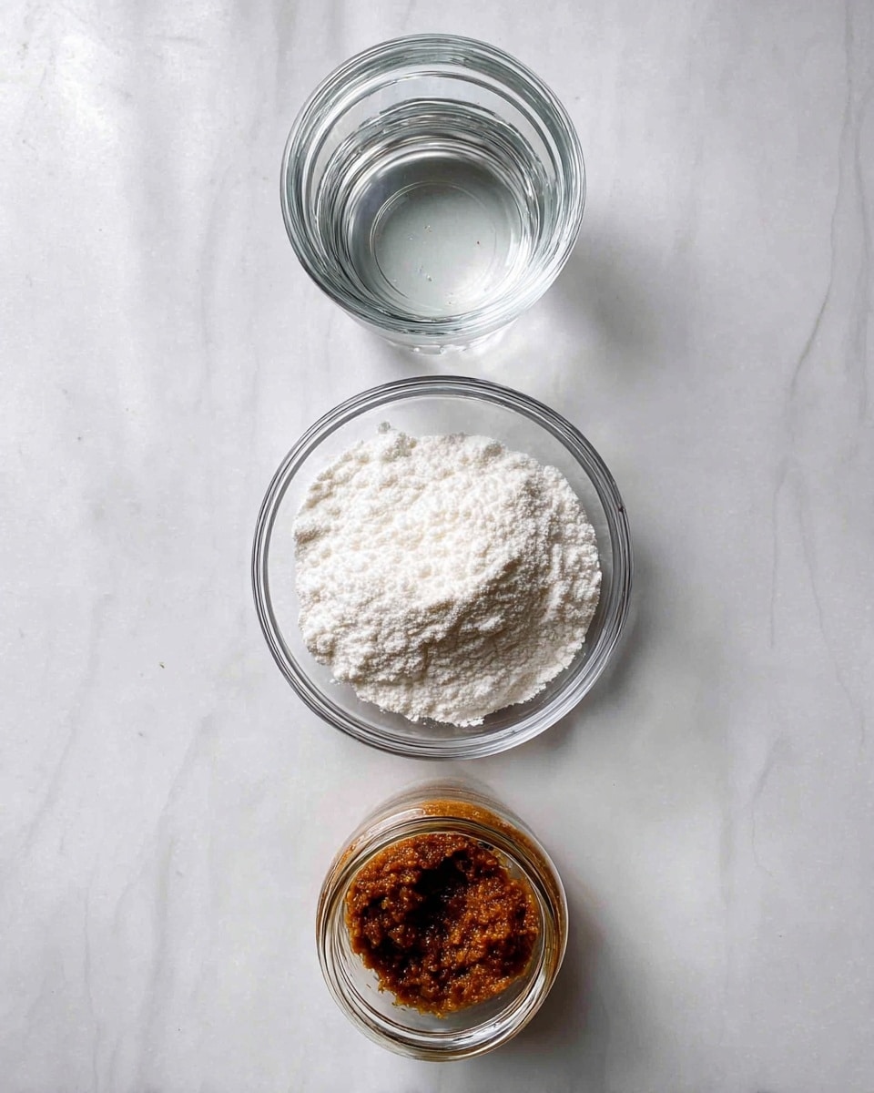 The image shows three containers arranged vertically on a white marbled textured surface, set in a top-down view. At the top, there is a clear glass jar filled with water, reflecting light softly. In the middle, a clear glass bowl holds a mound of white powdered substance with a fine, fluffy texture. At the bottom, an open glass jar contains a dark brown granular paste with a slightly sticky look. The composition is clean and simple, focusing on the textures and colors of the ingredients. photo taken with an iphone --ar 4:5 --v 7