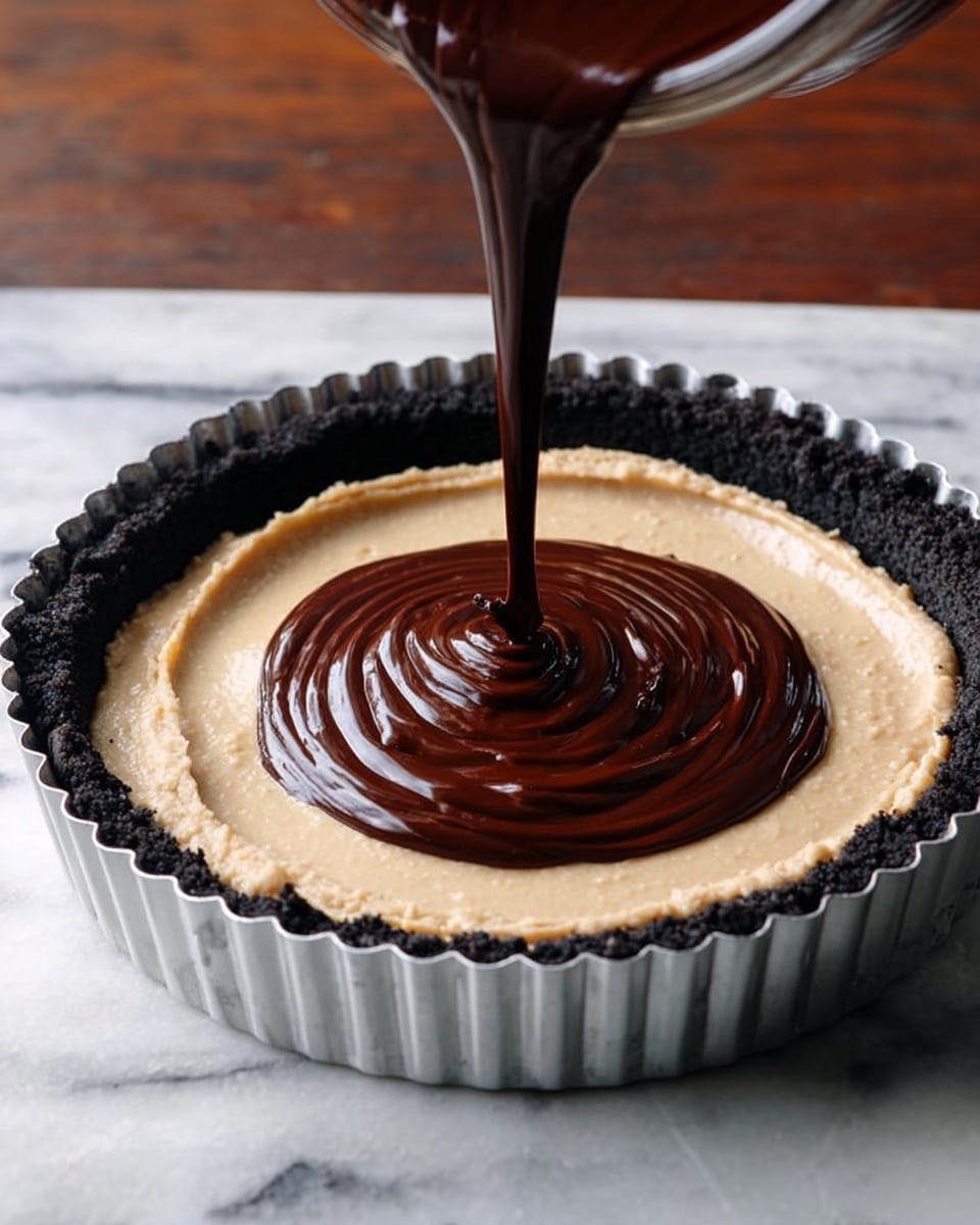 The image shows a tart with three clear layers inside a silver fluted tart pan placed on a white marbled surface. The bottom layer is a dark crumbly crust pressed against the sides, black in color. The middle layer is smooth and creamy, light beige, spread evenly over the crust. The top layer is dark chocolate sauce being poured in a thick spiral starting from the center, creating a shiny, rich texture contrasting with the creamy layer below. The photo taken with an iphone --ar 4:5 --v 7