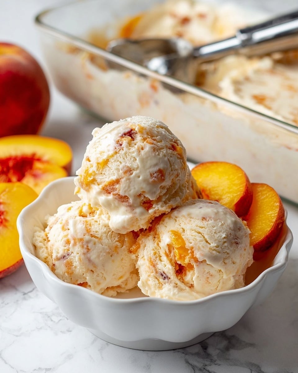 Three scoops of creamy peach ice cream with visible chunks of peach are placed in a white bowl with a scalloped edge. The ice cream is light off-white with swirls of orange peach throughout. On the right side of the bowl, there are two slices of bright orange-yellow peach. In the background, a clear rectangular glass dish filled with more of the same ice cream is partially visible, with a silver ice cream scoop resting on top. The scene is set on a white marbled surface. Photo taken with an iphone --ar 4:5 --v 7